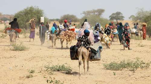 Sudanesische Flüchtlinge, die vor der Gewalt in der Region Darfur geflohen sind, suchen in Goungour, Tschad, vorübergehende Zuflucht. Das Bild zeigt Menschen, die zu Fuß und mit Eseln unterwegs sind und Gepäck tragen.