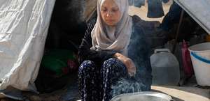 Eine Frau sitzt beim Kochen vor zwei Töpfen draußen vor einem Zelt