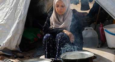 Famine in Gaza: A woman sits in front of two pots while cooking