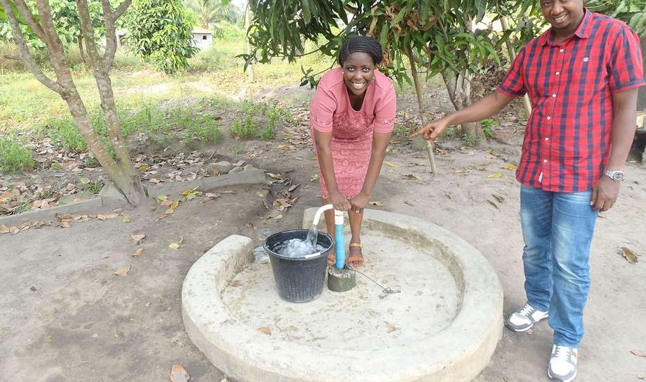 Eine Frau und ein Mann stehen an einer Wasserpumpe, Sierra Leone 2021.