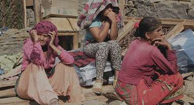 Two women and one girl are sitting in front of a damaged house