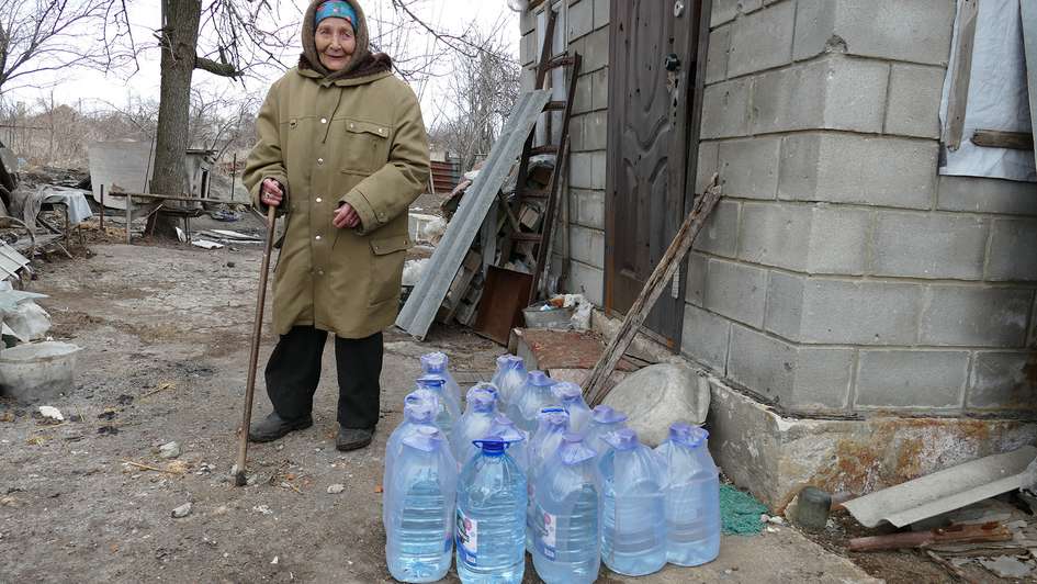 Eine Frau steht neben Wasserkanistern, Ukraine 2022.
