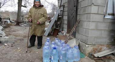 Eine Frau steht neben Wasserkanistern, Ukraine 2022.