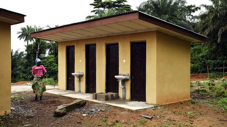 A woman is walking by a toilet house.