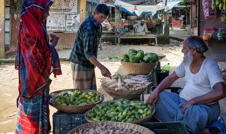 Eine Frau und ein Mann begutachten Gemüse bei einem Marktverkäufer in Bangladesch.