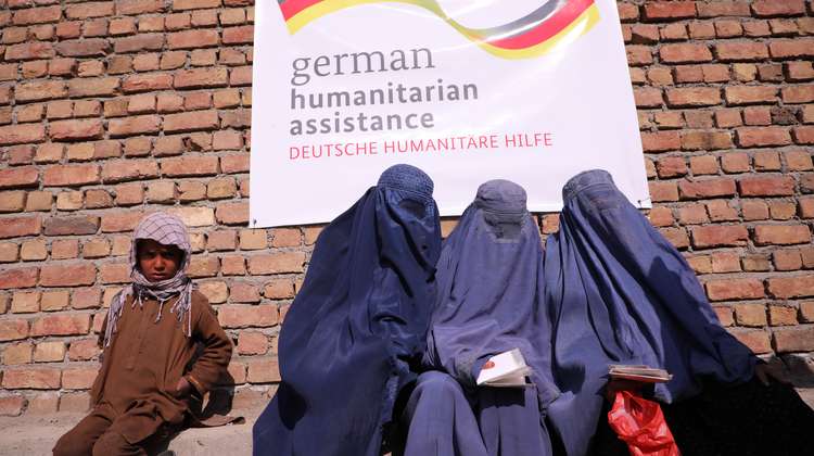 Drei Frauen mit blauen Burkas und ein Junge warten bei einer Lebensmittelverteilung in Kabul, Afghanistan. 