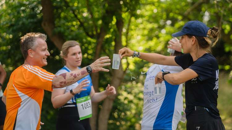 Eine Helferin reicht Läufern Becher mit Wasser