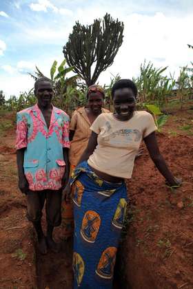 Mélanie Bacanurwanko (centre) with her husband and their daughter. Their field is steeply sloped and rocky; torrential rain has already eroded a lot of good soil.