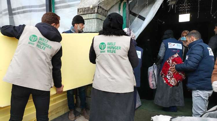 Welthungerhilfe staff members carry foam mattresses into an emergency shelter.