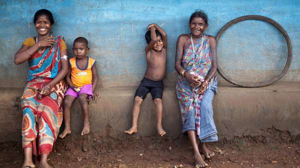 Zwei Frauen in Indien sitzen in traditionellen Gewändern mit Kindern auf dem Dorfplatz.