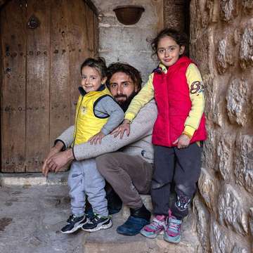 Ein Familienvater und zwei seiner Kinder im Flur eines Hauses aus Stein.