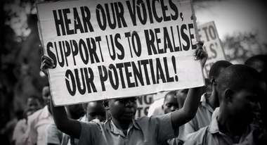 Child holding a sign that says "Hear our voices, support us to realise or potential!"