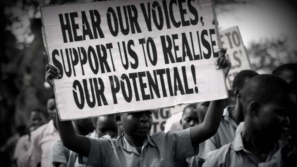 Child holding a sign that says "Hear our voices, support us to realise or potential!"