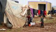 Two boys standing in front of a tent in a refugee camp in Idlib.
