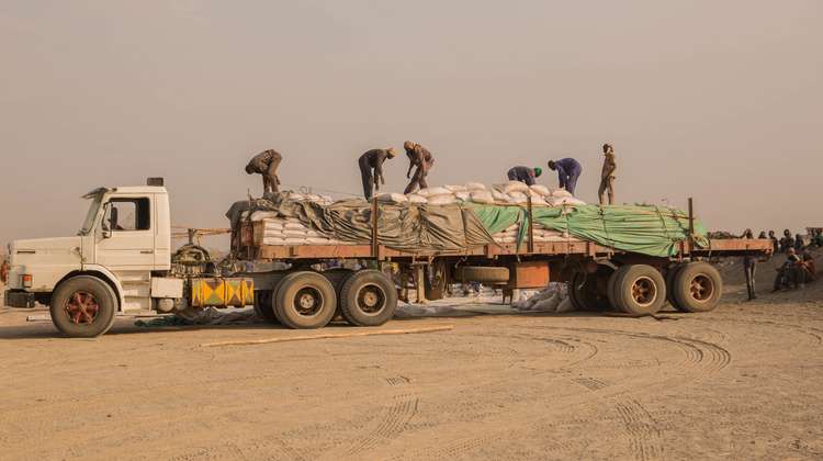 Sechs Menschen stehen auf einem Lastwagen und entladen Säcke voller Hirse, Südsudan 2018.