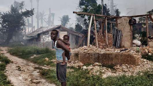 A man with his daughter in front of the remains of a house in Grand Anse.