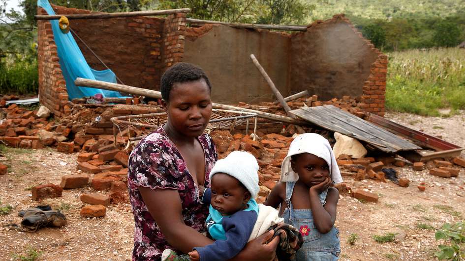 A woman and her children sitting in front of a house destroyed by cyclone Idai