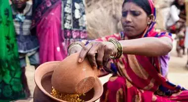 A woman in a sari holding a clay jar filled with food.