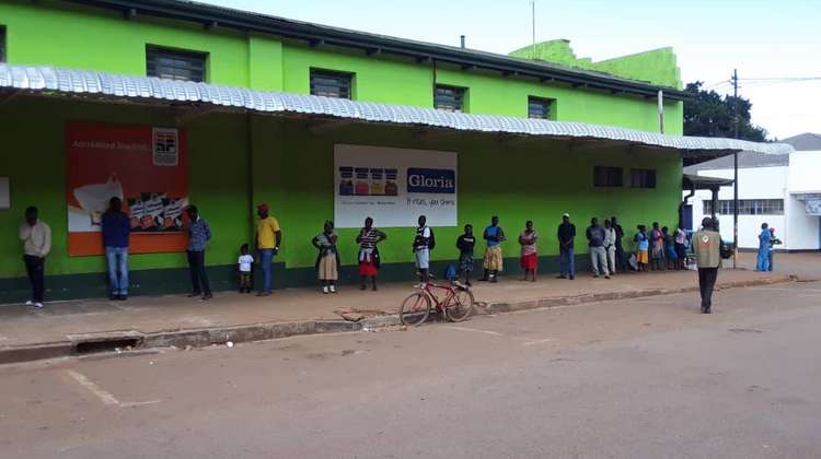 People standing in line in front of a supermarket in Zimbabwe and keeping their distance because of COVID-19.