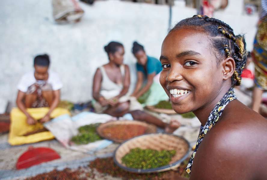 Girls and women working in a pepper factory, a girl in the foreground smiles at the camera