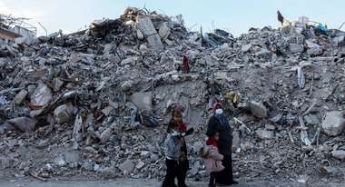 Eine Familie im türkischen Hatay steht nach den Erdbeben 2023 vor großen Trümmerbergen.