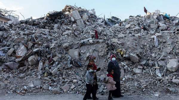 Eine Familie im türkischen Hatay steht nach den Erdbeben 2023 vor großen Trümmerbergen.