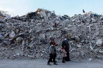 Eine Familie im türkischen Hatay steht nach den Erdbeben 2023 vor großen Trümmerbergen.
