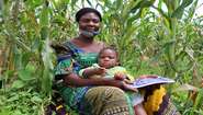 Eine Frau sitzt mit ihrem Kleinkind am Rande eines Maisfeldes, Kongo 2021.