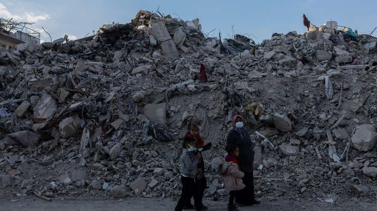 Eine Familie im türkischen Hatay steht nach de. Erdbeben 2023 vor großen Trümmerbergen.