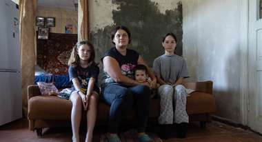 Eine Mutter und ihre drei Kinder sitzen für ein Portraitfoto auf einem Bett.