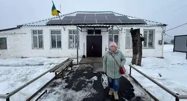 A woman in winter clothing stands in the snow in freezing temperatures in front of a house