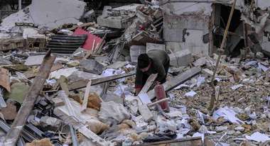 Krieg in der Ukraine. Bild: Ein Mensch inmitten von Trümmern, im Hintergrund sieht man ein zerstörtes Haus.