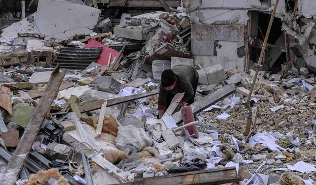 Krieg in der Ukraine. Bild: Ein Mensch inmitten von Trümmern, im Hintergrund sieht man ein zerstörtes Haus.