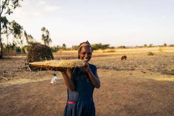Eine Frau hält ein eine große Platte mit geerntetem Getreide in der Hand