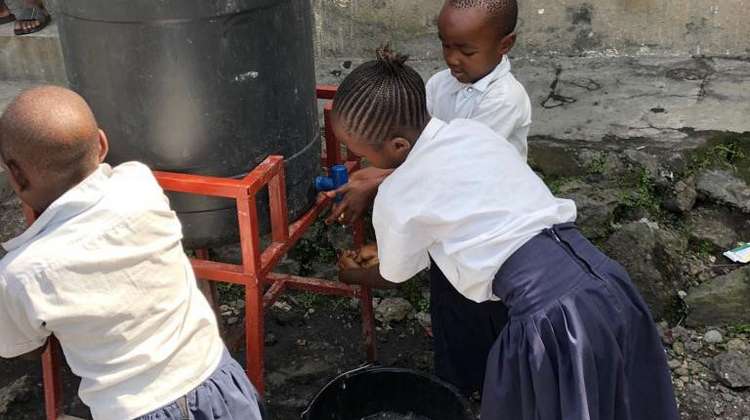 Schulkinder waschen sich an einem kleinen Wassertank die Hände.