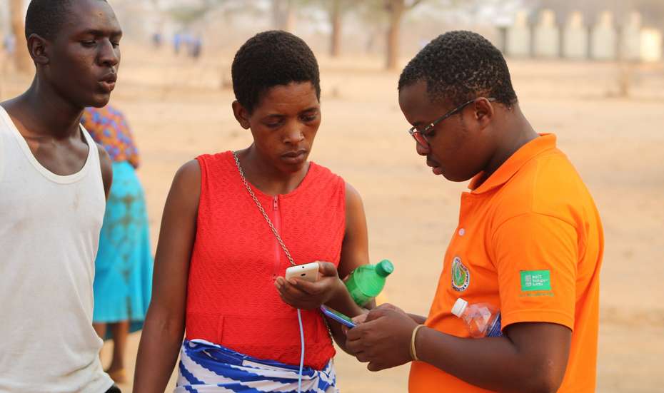 Zwei Männer und eine Frau mit einem Smartphone in der Hand, Simbabwe 2021.
