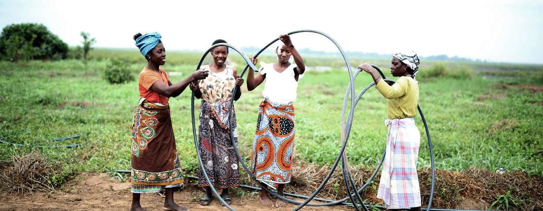 vier Frauen verlegen Schläuche zur Bewässerung eines Feldes