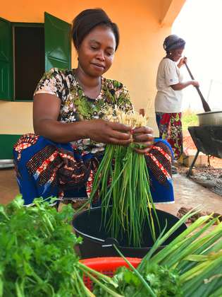 A woman sits on the floor cooking green vegetables