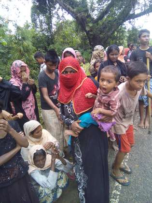 Rohingya auf der Flucht nach Bangladesch. Eine Mutter trägt ihr Kind auf dem Arm.