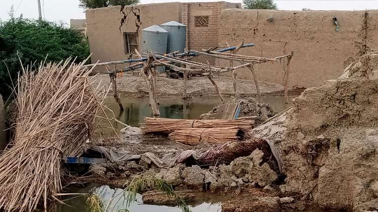 Überschwemmungen in Pakistan. Ein Haus aus Lehm mit Rissen in den Mauern, im Vordergrund ist Wasser und Schlamm zu sehen.