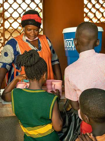 A woman distributes clean drinking water from a purifier to school children.
