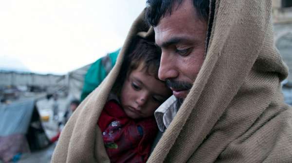 Vater sitzt mit Sohn zusammen in Decke eingehüllt im Flüchtlingscamp.