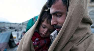 Vater sitzt mit Sohn zusammen in Decke eingehüllt im Flüchtlingscamp.
