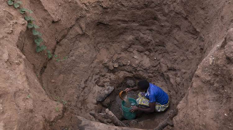 Eine Frau holt Wasser aus einem tiefen Loch in einem ausgetrockneten Fluss, Kenia 2021.