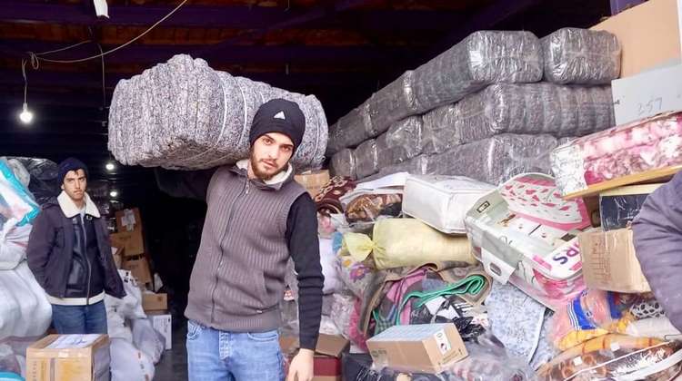 A young man carries a bundle of blankets from a storage room.