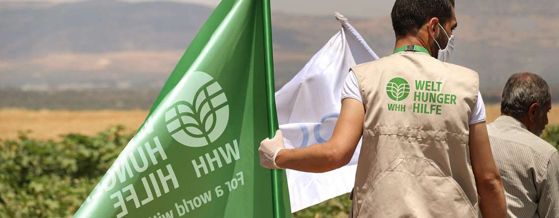 Ein Mann mit Welthungerhilfe-Weste hält eine grüne Flagge mit dem neuen Welthungerhilfe-Logo in der Hand.