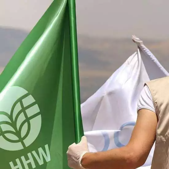 Ein Mann mit Welthungerhilfe-Weste hält eine grüne Flagge mit dem neuen Welthungerhilfe-Logo in der Hand.
