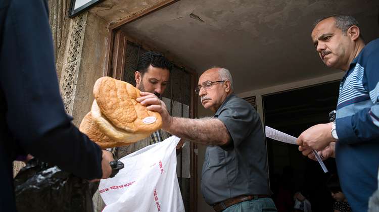 Men puts bread in a plastic bag of a refugee
