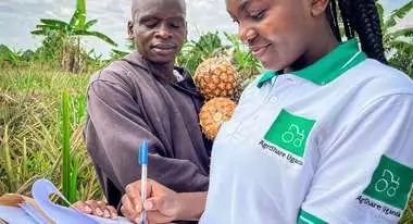 Titelfoto des Jahresbericht 2021. Eine Welthungerhilfe-Mitarbeiterin mit AgriShare-T-Shirt macht Notizen, während ein Mann im Hintergrund zuschaut. Er hält zwei Ananas in den Händen.