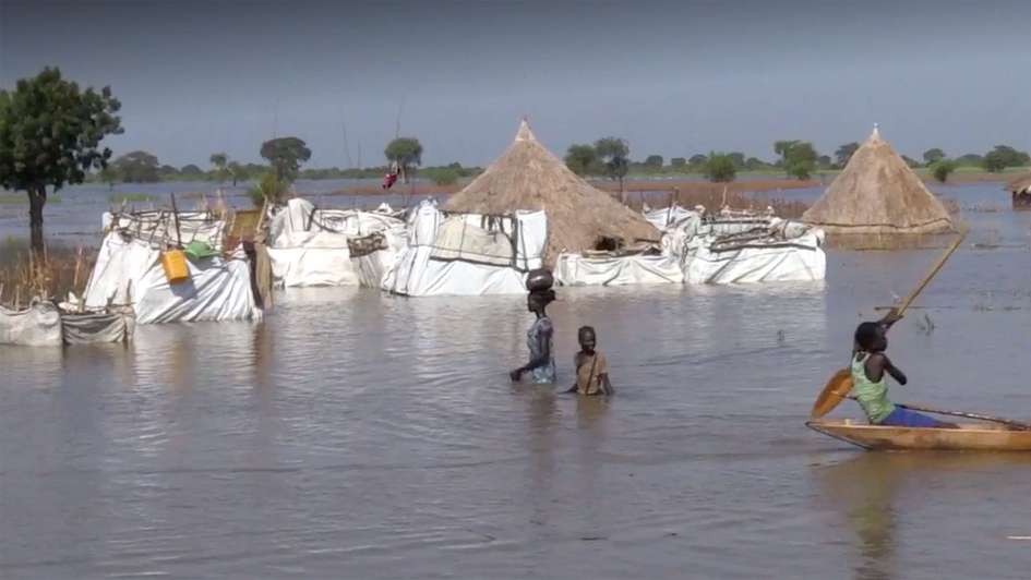 2021-ueberschwemmungen-nothilfe-suedsudan_C_welthungerhilfe.jpg Überschwemmungen im Südsudan: Eine Frau und ein Kind waten durch das hüfthohe Wasser, im Hintergrund sind überschwemmte Hütten zu sehen.